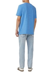 Blauwe T-shirt met korte mouwen in een gemêleerde textuur. Gecombineerd met lichtblauwe spijkerbroek en casual instapschoenen met donkere accenten.