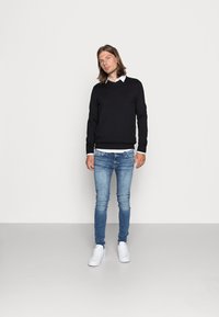 Sort sweater over en hvid skjorte med krave, parret med lyseblå skinny jeans og hvide sneakers. Glatte teksturer, enkelt design.