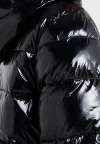 Lśniąca czarna kurtka puchowa z poziomym pikowaniem, pokazująca zbliżenie na ramię i górną część ramienia.