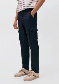 Mornarski cargo hlače s stranskimi žepi, narejene iz bombaža. Nosijo se z majico z navpičnimi črtami in bež teniskami. Imajo sproščen kroj in zožene noge.