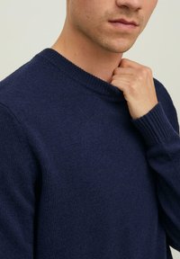 Granatowy sweter dziany z okrągłym dekoltem, ściągaczami na rękawach oraz fakturowanym wykończeniem. Zbliżenie koncentruje się na tkaninie i dopasowaniu.