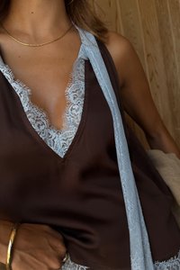 Top marrone senza maniche con scollatura a V, caratterizzato da un delicato bordo di pizzo azzurro chiaro lungo i bordi. Il tessuto morbido e i dettagli di pizzo raffinati arricchiscono il design.