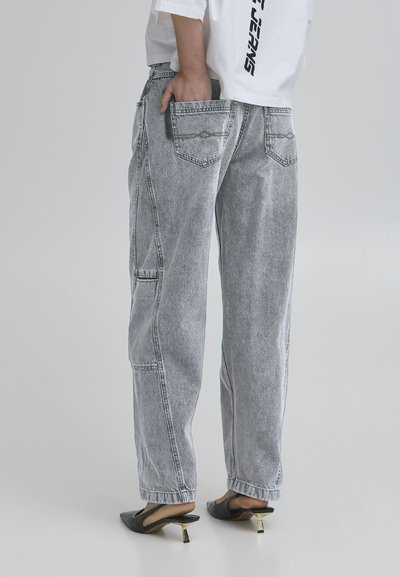Light gray denim jeans with a relaxed fit, featuring back pockets and a slightly faded texture. Paired with black heeled mules.