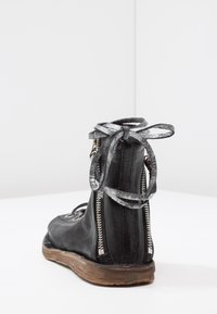 Black leather ankle boot with silver zipper at the back, metallic silver laces tied in a bow, and worn brown sole on white surface.