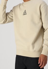 Felpa in cotone beige con maniche lunghe. Presenta un logo triangolare nero sul petto e polsini e orlo a coste.