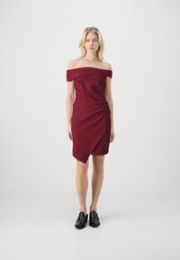 Burgundi off-the-shoulder mekko, jossa on tiukka keskiosa ja roikkuva, epäsymmetrinen helma. Yhdistetty mustiin kenkiin. Sileä kangas.