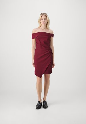 Burgundy off-the-shoulder dress featuring a fitted bodice and a draped, asymmetrical hem. Worn with black shoes. Smooth fabric texture.