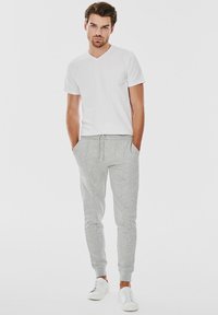 Biała koszulka z dekoltem w serek i szare spodnie dresowe z elastycznymi mankietami. Białe trampki. Materiał wydaje się miękki i wygodny. Prosty, minimalistyczny design.