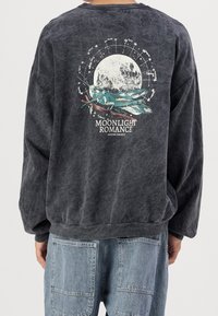 Grafiitinharmaa ylipitkä collegepaita, jossa on kuu- ja maisemakuva, sekä valkoisella ja punaisella teksti "Moonlight Romance". Pehmeä tekstuuri.