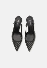 Talons hauts à bout pointu noirs avec des détails en œillets argentés. Tige en cuir lisse, talon plat et bride de cheville réglable.