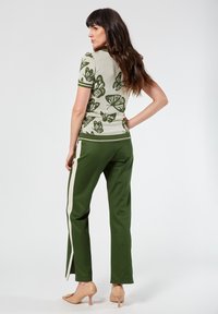 Top verde con estampado de mariposas y mangas cortas, con detalles acanalados, combinado con pantalones verdes que tienen una franja lateral color crema y tacones neutros.