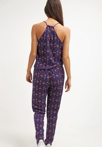 Combi-short sans manches en tissu bleu foncé avec des motifs géométriques rouges et blancs. Présente un dos nageur et une taille élastique.