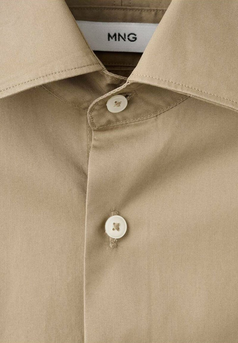 Beige overhemd met een klassieke kraag, voorzien van twee witte knopen en een gladde stoftextuur. Het label zegt "MNG."