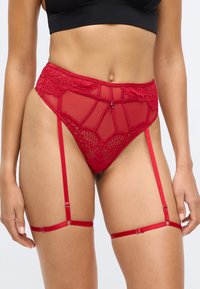 Soutien-gorge en dentelle rouge et en résille avec des bretelles ajustables et des motifs floraux délicats. Doté d'un design sans couture et d'accents en matériel brillant.