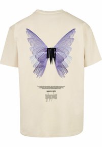 Camiseta de algodón color crema con un gran gráfico de mariposa morada y texto negro en la parte posterior, con patrones detallados en las alas y un cuello redondeado.