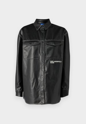 Giacca camicia in ecopelle nera con chiusura a bottoni, due tasche sul petto, cuciture bianche a contrasto e un logo sul lato sinistro.