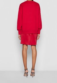 Felpa rossa oversize con maniche lunghe, cuciture in vista, abbinata a una gonna di raso rossa e sandali argentati con tacco alto.