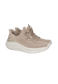 Zapatillas deportivas beige con una parte superior de malla texturizada, cierre de cordones y una suela blanca acolchada acentuada con un sutil detalle metálico.