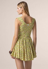 Abito giallo senza maniche con gonna a ruota, dotato di un motivo floreale in rosa e verde. Tessuto liscio e dettaglio con scollatura rotonda.