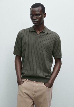 Knit polo shirt in dark green with vertical ribbing, short sleeves, and a classic collar; paired with light beige trousers.
