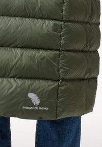 Olivgrüne Steppdaunenjacke mit horizontalen Steppungen, versehen mit einem weißen "PREMIUM DOWN"-Logo am Saum. Texturiertes, leichtes Material.