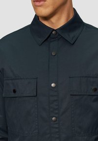 Granatowa koszula overshirt wykonana z lekkiego materiału, z kołnierzykiem w szpic, zatrzaskami oraz dwiema kieszeniami na piersi z klapami.