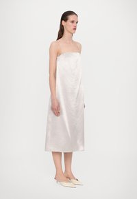 Satin midi haljina u mekom srebrnom tonu s tankim naramenicama, koja ima opušteni kroj i glatku teksturu, upotpunjena sypim cipelama na špic.
