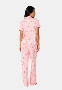Roze pyjama set met een knoopsluiting korte mouwen shirt en lange broek met een speelse print van harten, bloemen en eenhoorns.