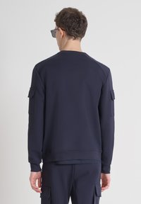 Sudadera azul marino con cuello redondo, mangas largas y parches en los hombros. Tejido suave, puños acanalados y un corte relajado.
