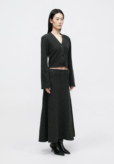 Σκούρο γκρι, πλεκτό δίχρωμο σύνολο που περιλαμβάνει ένα κοντό cardigan με κουμπιά και μια μακριά φούστα σε συνδυασμό με μαύρες μπότες με τακούνι.