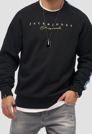 Sudadera negra con "JACK & JONES Originals" en texto blanco y amarillo. Presenta mangas raglán y acentos azules en las mangas.