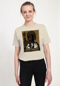 Béžové tričko s grafickou potiskem Boba Fetta, Hana Sola a R2-D2 s nápisem "Impérium vrací úder"; krátké rukávy, volný střih.