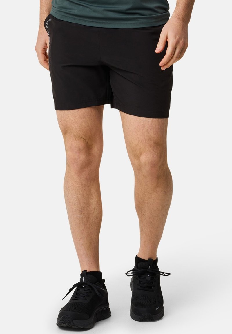 Svarta atletiska shorts med en mjuk textur, mitt på låret längd och en åtsittande design, kombinerat med svarta snörade sneakers.