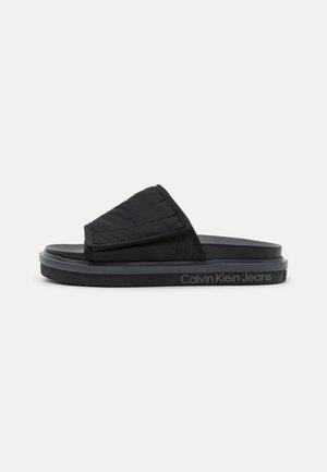 Czarna klapka Calvin Klein Jeans z wyściełanym górnym paskiem i grubą podeszwą, widoczna z boku na białym tle.