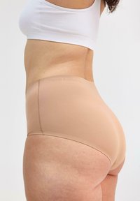 Beige sömlös underkläder med hög midja och en jämn textur. Diskret branding längs midjebandet, med minimal sömnad.