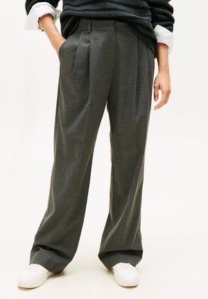 Grijze geplooide broek met een op maat gemaakte pasvorm, gemaakt van een textuurstof, met zijzakken en een ontspannen silhouet. Draagt met witte sneakers.