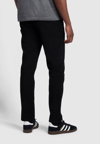 Schwarze Cordhosen mit einer taillierten Silhouette, kombiniert mit schwarz-weißen Sportschuhen. Die Textur der Hosen ist gerippt.