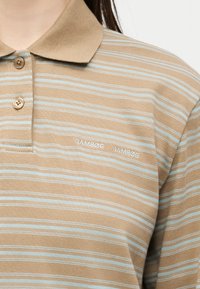 Polo beige et bleu clair à rayures avec trois boutons et "SAMSOE SAMSOE" brodé sur la poitrine gauche.