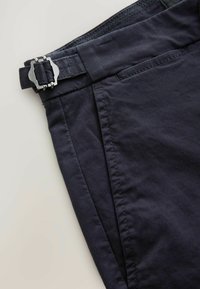 Pantalones azul marino oscuro con una textura suave, con un frente plano y una hebilla de metal plateado en la cintura para ajuste.
