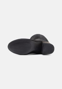 Bottine en daim noir avec petit talon carré vue de la semelle, dotée d'une semelle extérieure en caoutchouc antidérapante texturée et d'une base de talon lisse.