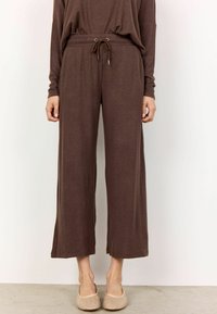 Bruine wijdvallende broek met een trekkoord in de taille en ribbelstructuur. Ze hebben zijopeningen voor meer bewegingsvrijheid en een ontspannen pasvorm.