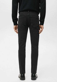 Vaqueros de mezclilla negros, corte slim, con dos bolsillos traseros y detalles mínimos de costura, combinados con zapatos negros y una camisa negra de manga larga.