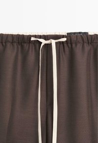 Pantaloni marroni con vita elastica e coulisse bianca. Tessuto leggero dalla texture liscia e design semplice.