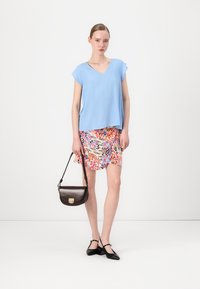 Top blu chiaro a V, mini gonna a fantasia colorata, borsa nera con accessori dorati e scarpe nere basse. Tessuto morbido, vestibilità comoda.