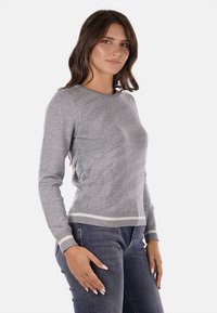 Maglione grigio lavorato a maglia con un design testurizzato, colletto rotondo e leggere strisce all'acromo e all'orlo, abbinato a jeans scuri.