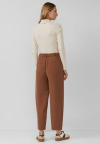 Beżowa bluzka z długim rękawem i wysokim kołnierzem, zestawiona z brązowymi spodniami zwężanymi, z elastycznym paskiem w talii i dwoma tylnymi kieszeniami.
