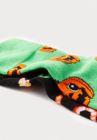 Chaussettes vertes avec un motif de visage de tigre orange, dotées d'un orteil et d'un talon noirs. Fabriquées en tissu doux, affichant une texture côtelée.