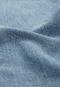 Tejido de mezclilla azul claro con un tejido de sarga, que presenta una textura suave y un sutil patrón de costillas diagonales. La superficie es lisa y uniforme.
