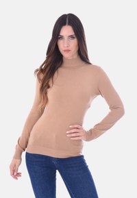 Maglione a collo alto beige realizzato in un morbido tessuto lavorato a maglia. Presenta maniche lunghe e polsini a coste, abbinato a jeans blu.