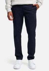 Chinos azul marino de tela ligera, con un diseño de pierna recta, frente plano, bolsillos laterales y combinados con zapatillas blancas.